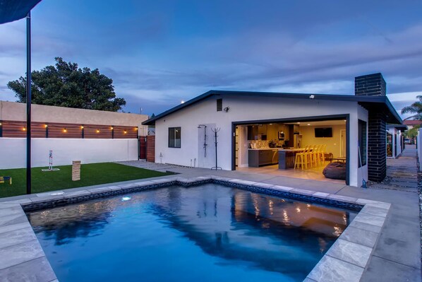 A modern house with a swimming pool, a bar area, and a well-maintained lawn.