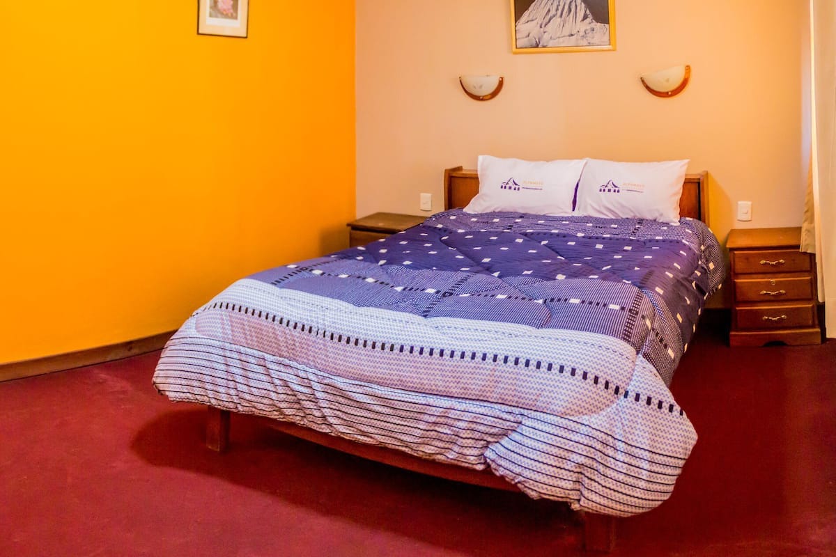 Ein ordentlich bezogenes Bett mit einem gemusterten Überwurf, ein gerahmtes Bild an der Wand und ein kleiner Nachttisch mit Lampe.