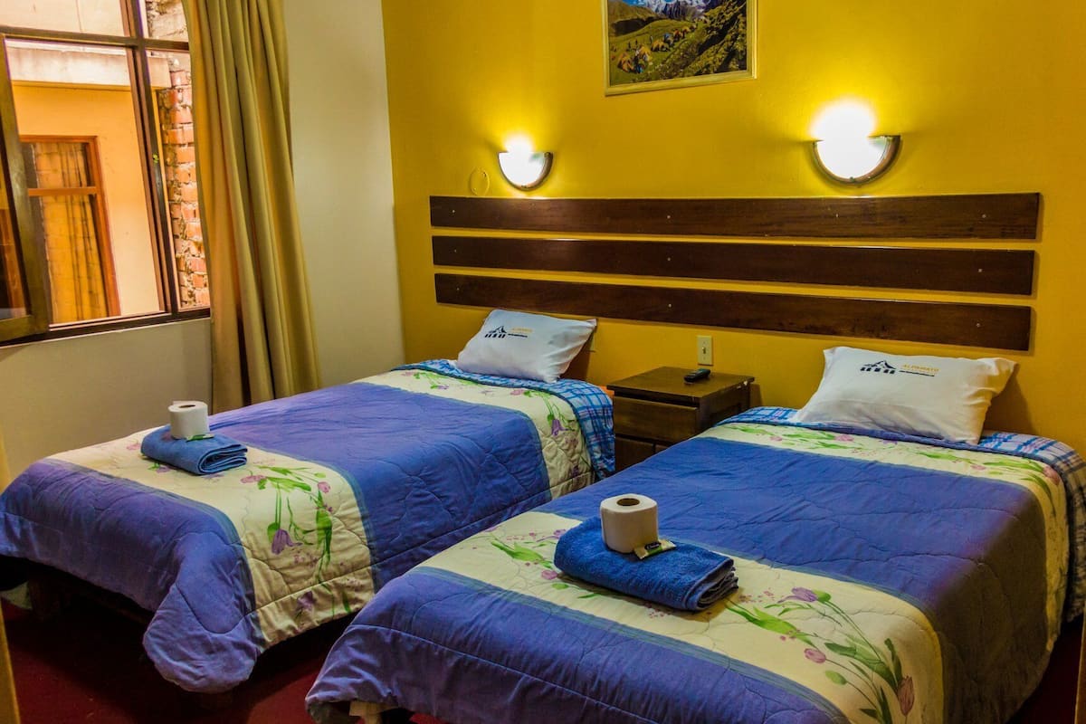 Ein Hotelzimmer mit zwei Betten, jedes mit einem blauen und floralen Überwurf, einem Holz-Kopfteil und einem Gemälde über den Betten.