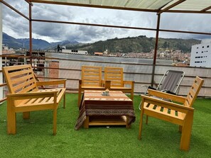 An outdoor seating area with wooden furniture and a table, set on artificial grass, overlooking a cityscape with mountains in the distance. - Alpamayo Guest House (Huaraz)
