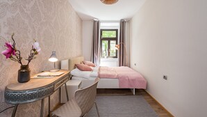 Un dormitorio con cama, mesita de noche, lámpara y ventana con cortinas.