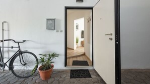 Una entrada limpia y moderna con una bicicleta, una planta en maceta y una puerta que da paso a un interior con piso de madera.