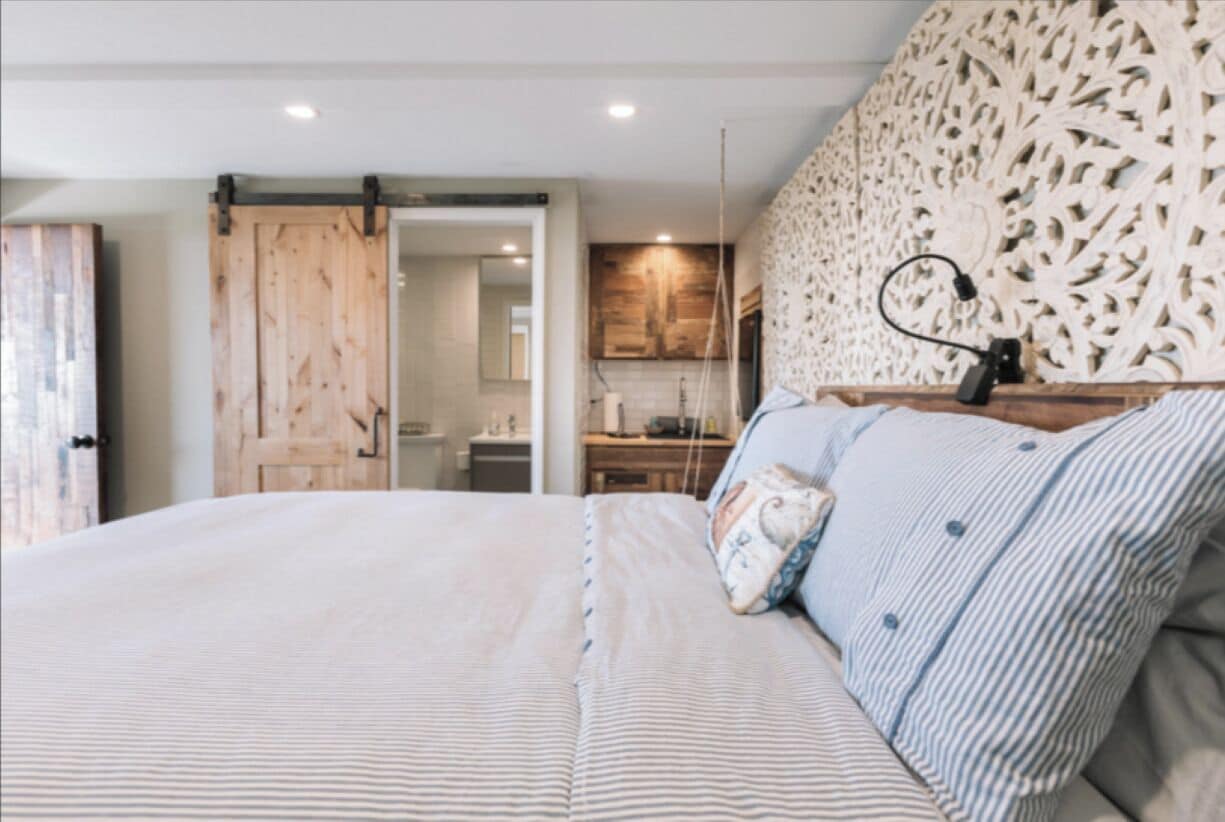 Une chambre avec un grand lit, une porte en bois et un coin cuisine visible à travers une porte ouverte.
