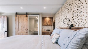 A bedroom with a large bed, a wooden door, and a kitchen area visible through an open door. - Private Studio , spectacular  Ocean View , bathroom , kitchenette, Very Quiet (Half Moon Bay)
