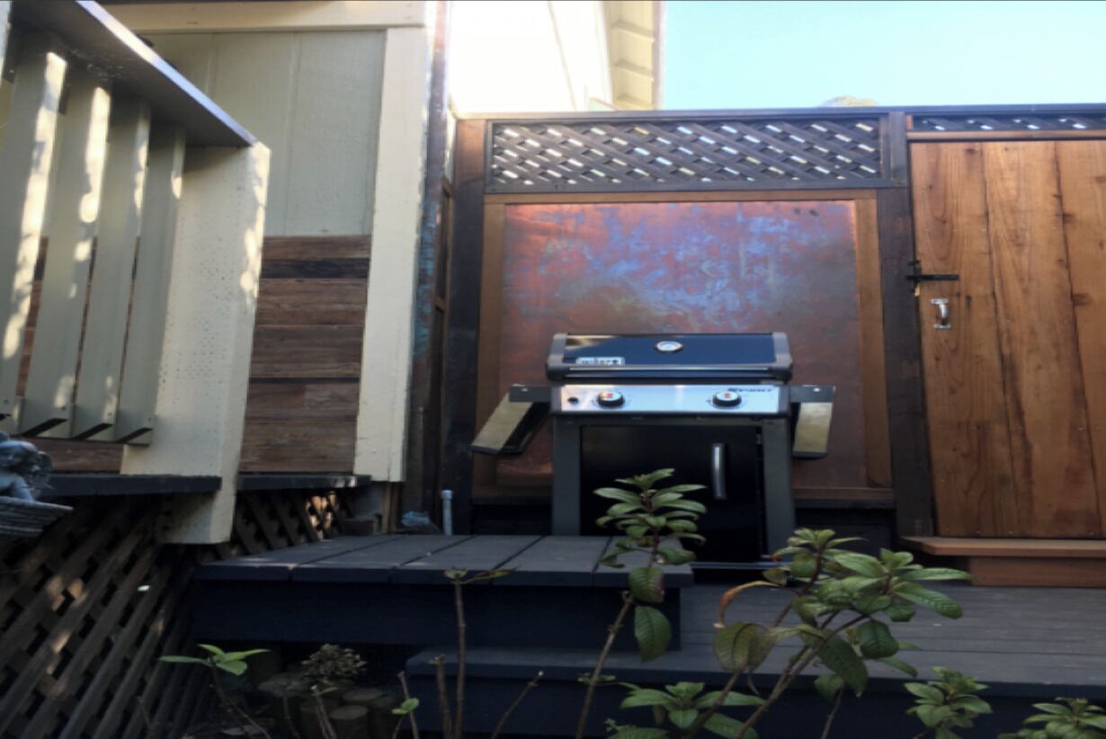 Un patio con una parrilla, una puerta de madera y un portón de metal.