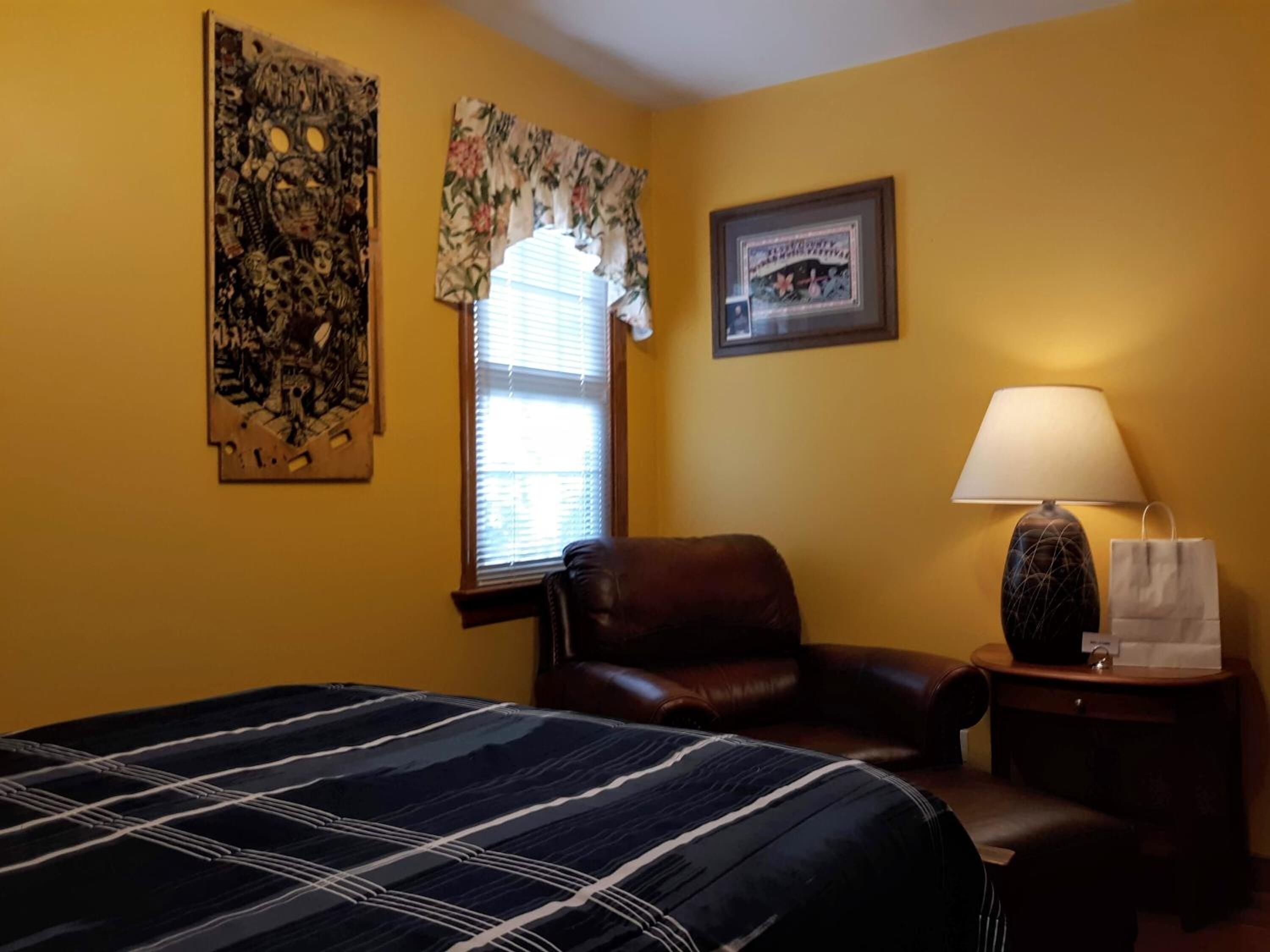 A hotel room with a bed, a leather chair, a lamp, and a window with blinds.