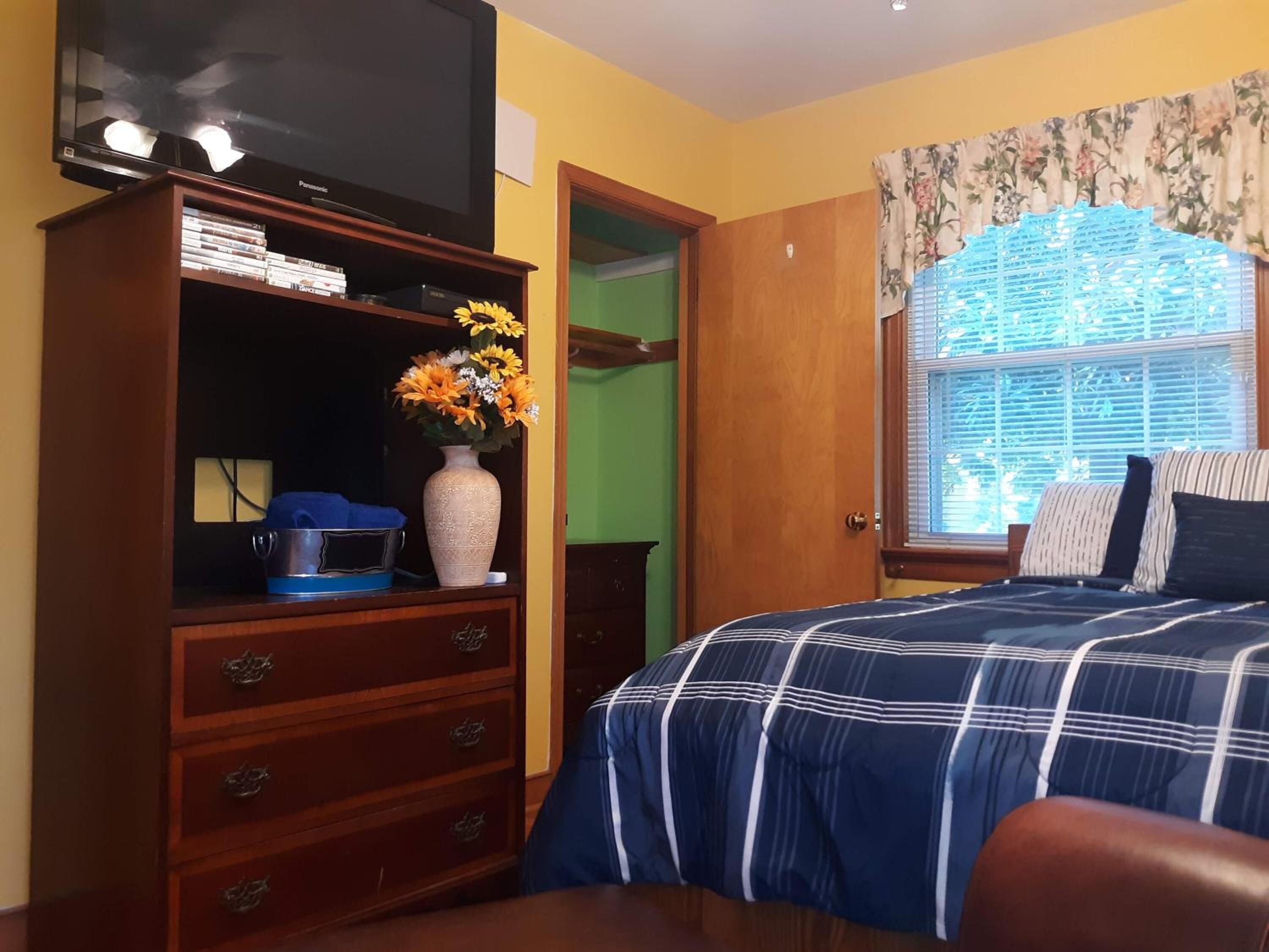 Un dormitorio con cama, cómoda, televisor y ventana con persianas.
