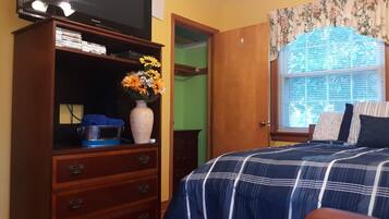 Un dormitorio con cama, cómoda, televisor y ventana con persianas.