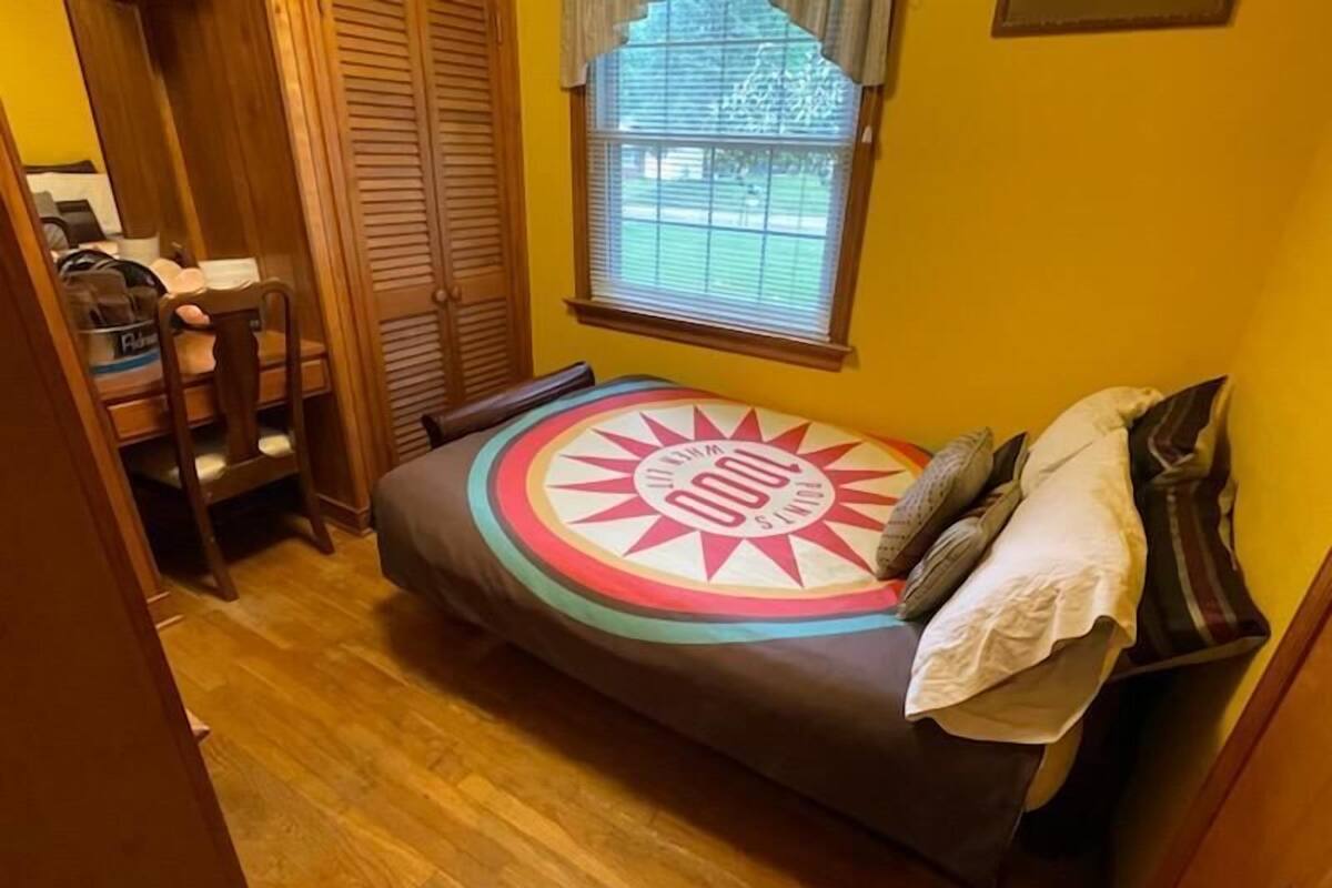 Une petite chambre à coucher, chaleureuse et accueillante, avec un lit, une fenêtre et une armoire en bois.