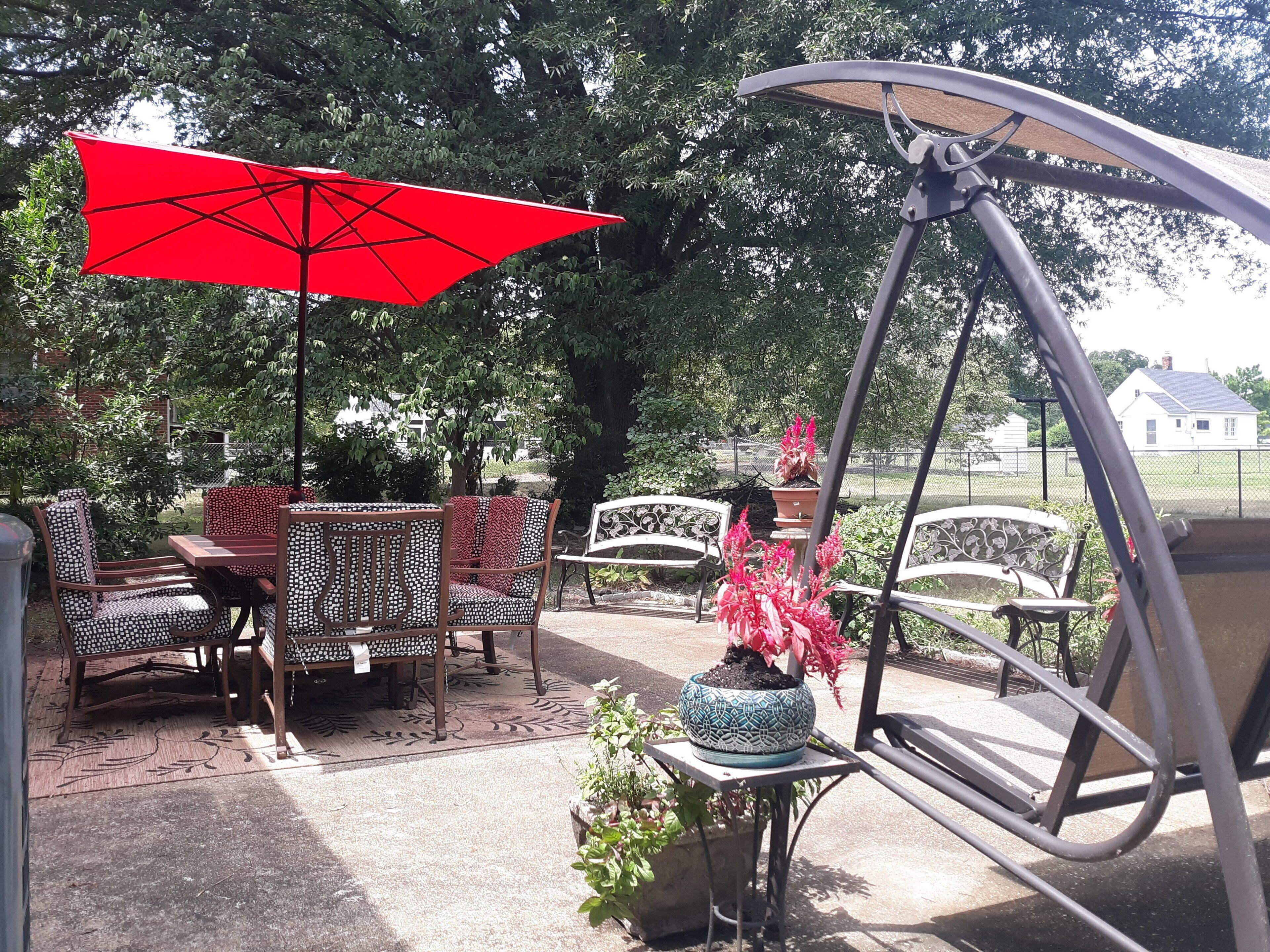 An outdoor patio area with a swing chair, a table with chairs, and a red umbrella.