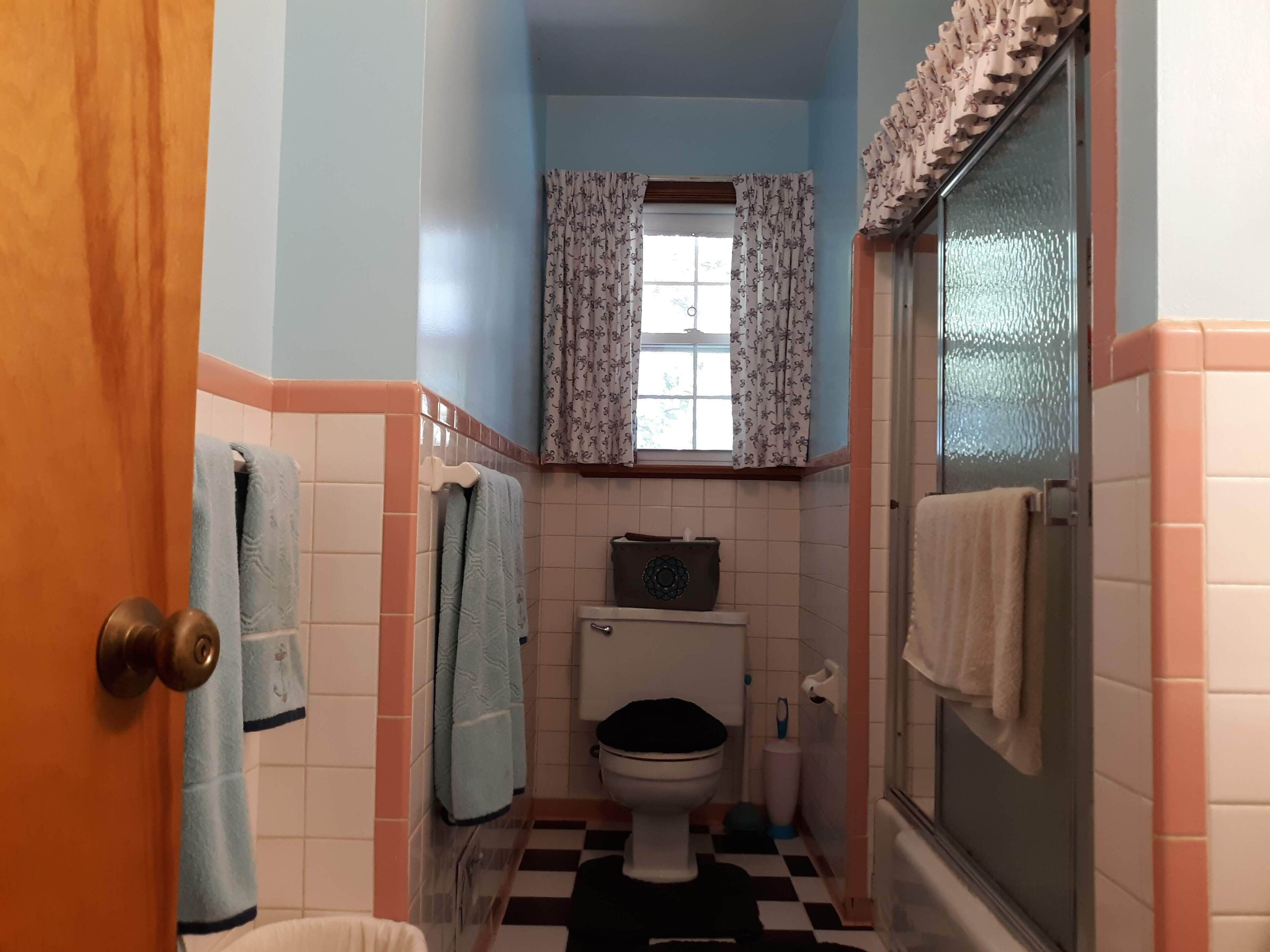 A small bathroom with a toilet, a window with patterned curtains, and a shower area.