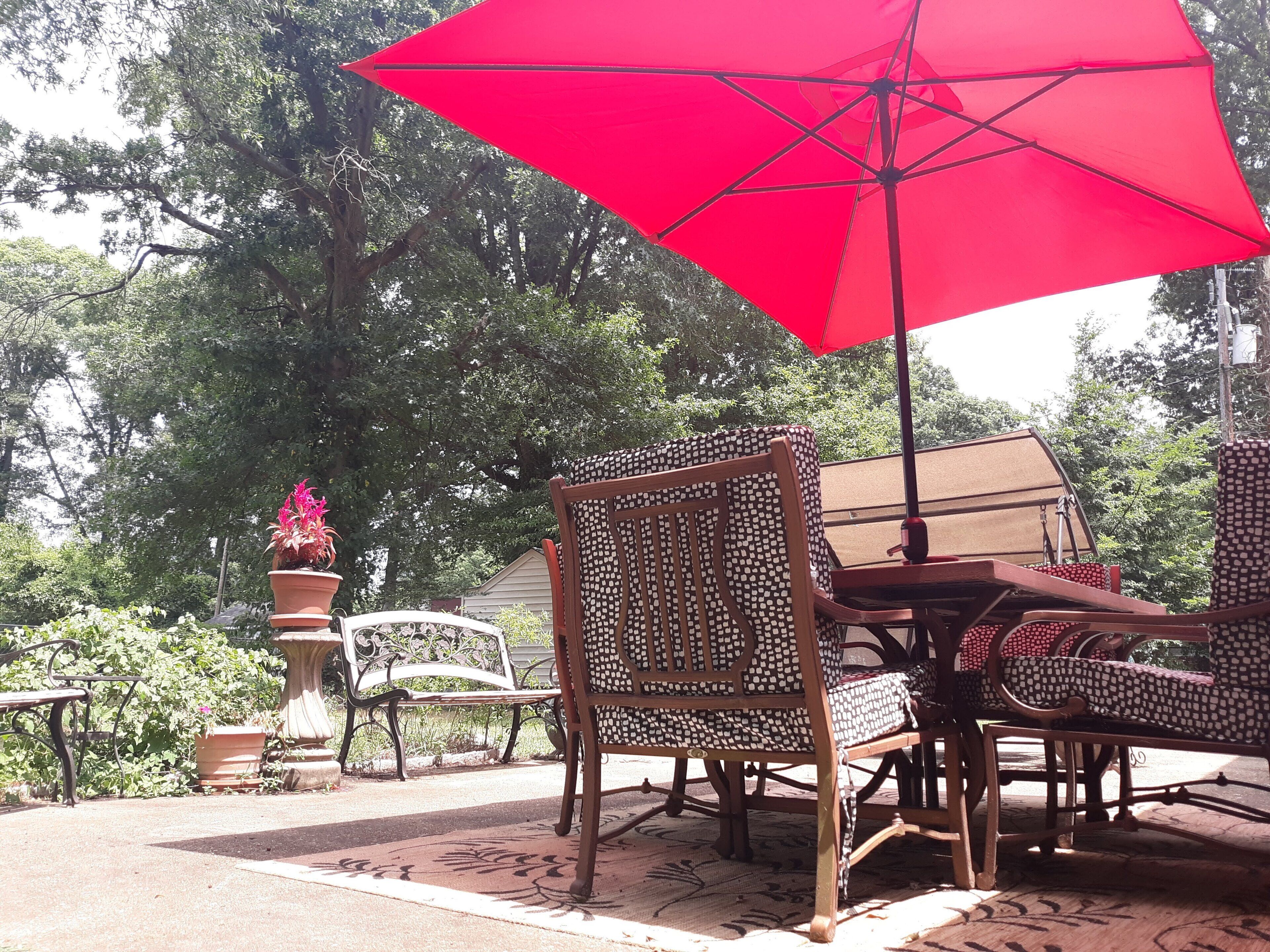 An outdoor patio with wicker furniture, a red umbrella, and potted plants.