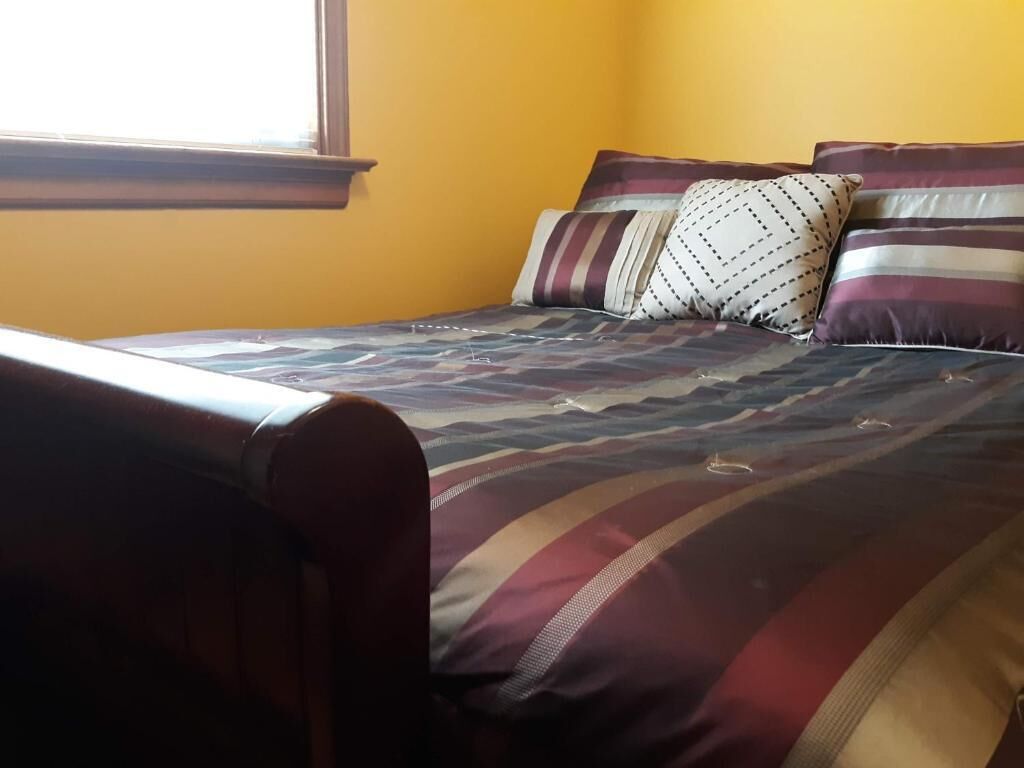 Een bed met een beddengoed met patroon en meerdere kussens in een kamer met gele wanden.