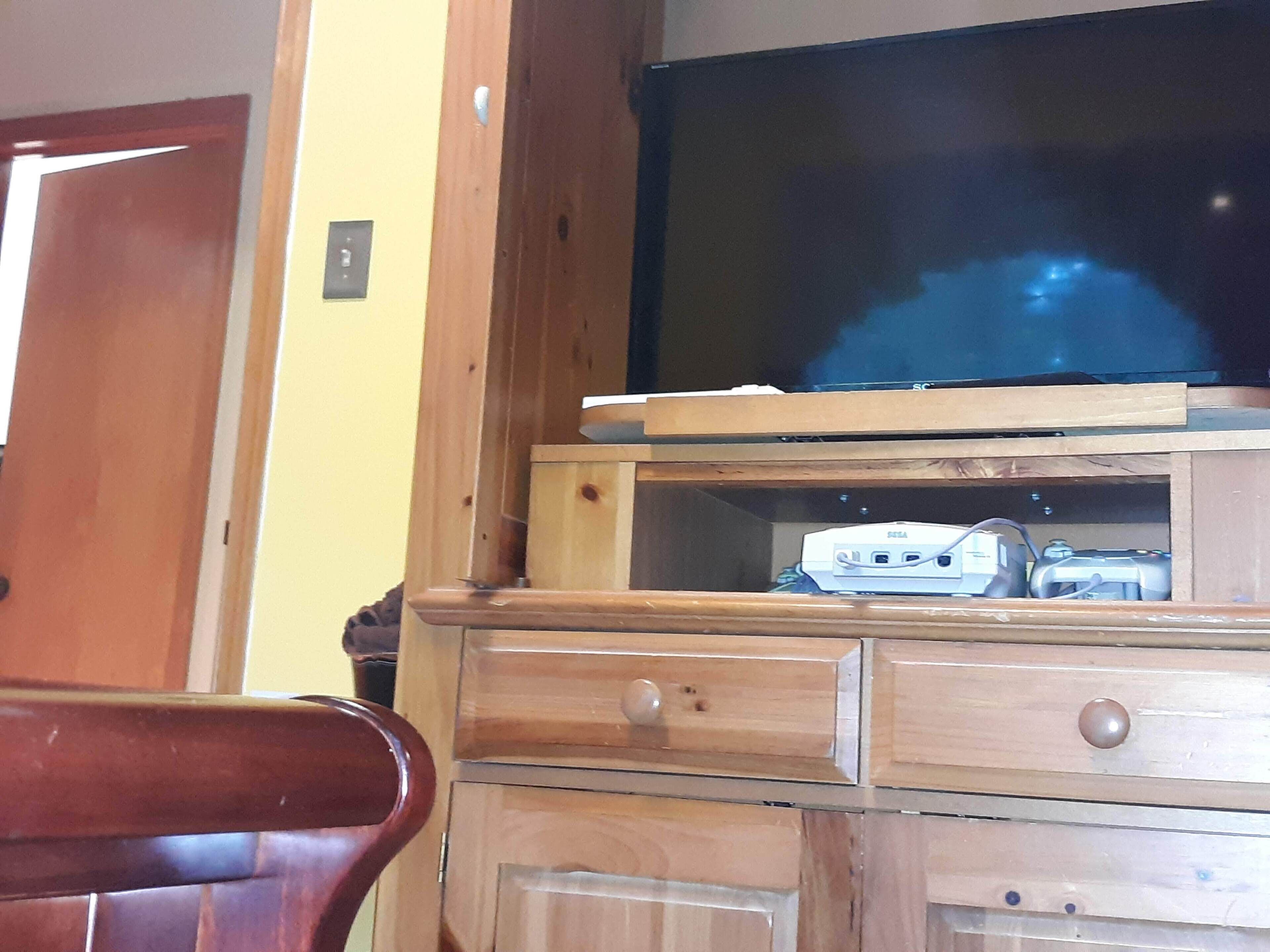 A wooden entertainment center with a television, a gaming console, and drawers.