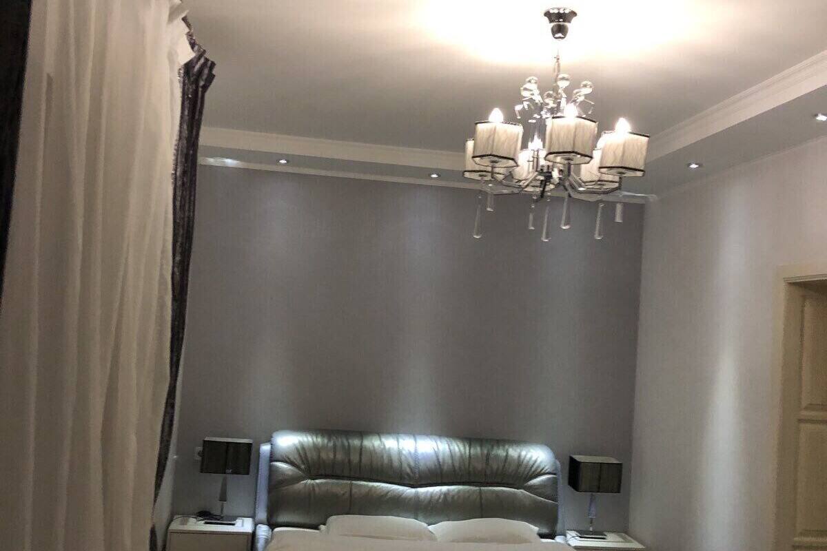 A bedroom with a large bed, a chandelier, two bedside tables with lamps, a chair, and a door.