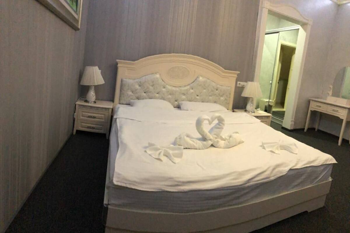 A neatly made bed with a white headboard and footboard, a bedside table with a lamp, and a mirror on the wall.