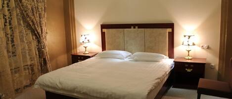 Una cama bien hecha con sábanas blancas, dos mesitas de noche con lámparas y una silla.