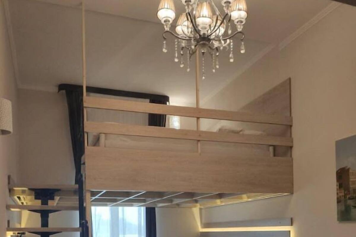A loft-style bedroom with a bunk bed, a staircase, a sofa, a round table, and a chandelier.