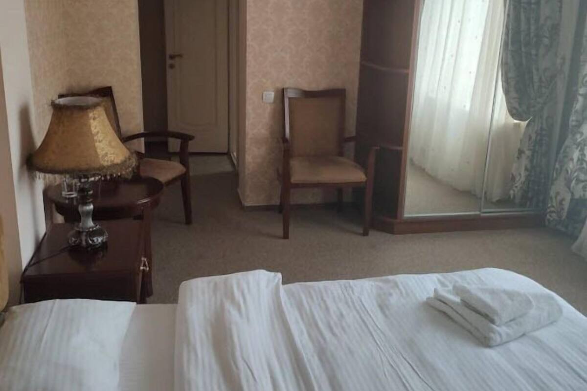 A hotel room with a bed, a chair, a lamp, and a large mirror.