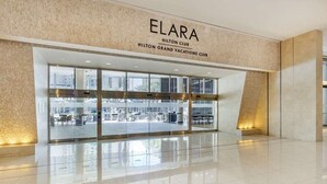 The entrance to the Elara Hilton Club with a modern design, large glass windows, and a clean, reflective floor.