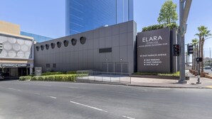 A modern building with a sign for the Elara Hilton Club, including amenities like valet parking and a self-park area.