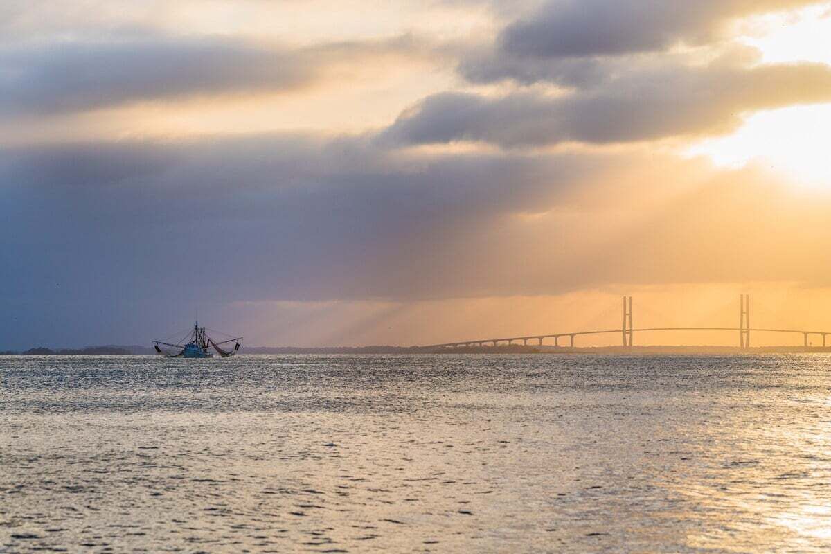 Un plan d’eau calme, avec un bateau de pêche et un pont au loin.
