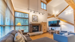 A spacious living room with a fireplace, a large TV mounted on the wall, and a cozy seating area with sofas and a blue armchair. - Keystone Townhome in Quiet Location Near Resort Shuttle, Access to Activities (Keystone)