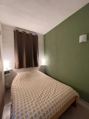 A bedroom with a bed, two bedside lamps, a nightstand, a curtain, and a wall-mounted light fixture.