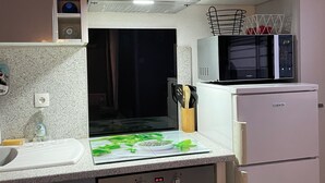 Una cocina con microondas, horno y una encimera con tabla de cortar y utensilios.
