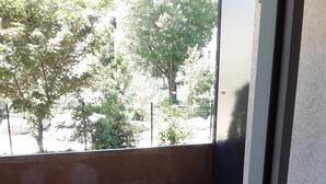 Un balcón con una mesa y dos sillas, vista a árboles y un edificio al fondo.