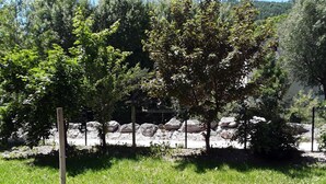 Vista al borde de la carretera con un área verde, árboles y una cerca de rocas al fondo.