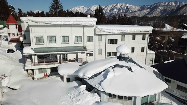 A multi-story building with snow-covered roofs and a mountainous backdrop. - The Phat Packers - Hostel (Otari)