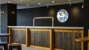 A modern kitchen with a black brick wall, wooden cabinets, and a stainless steel sink. - The Phat Packers - Hostel (Otari)