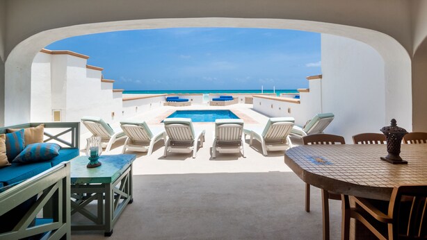 Un espace aménagé au bord de la piscine, avec des chaises longues, une table et une vue sur l’océan.