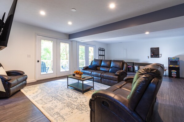 A spacious living room with a leather sofa, a coffee table, and a flat-screen TV mounted on the wall.