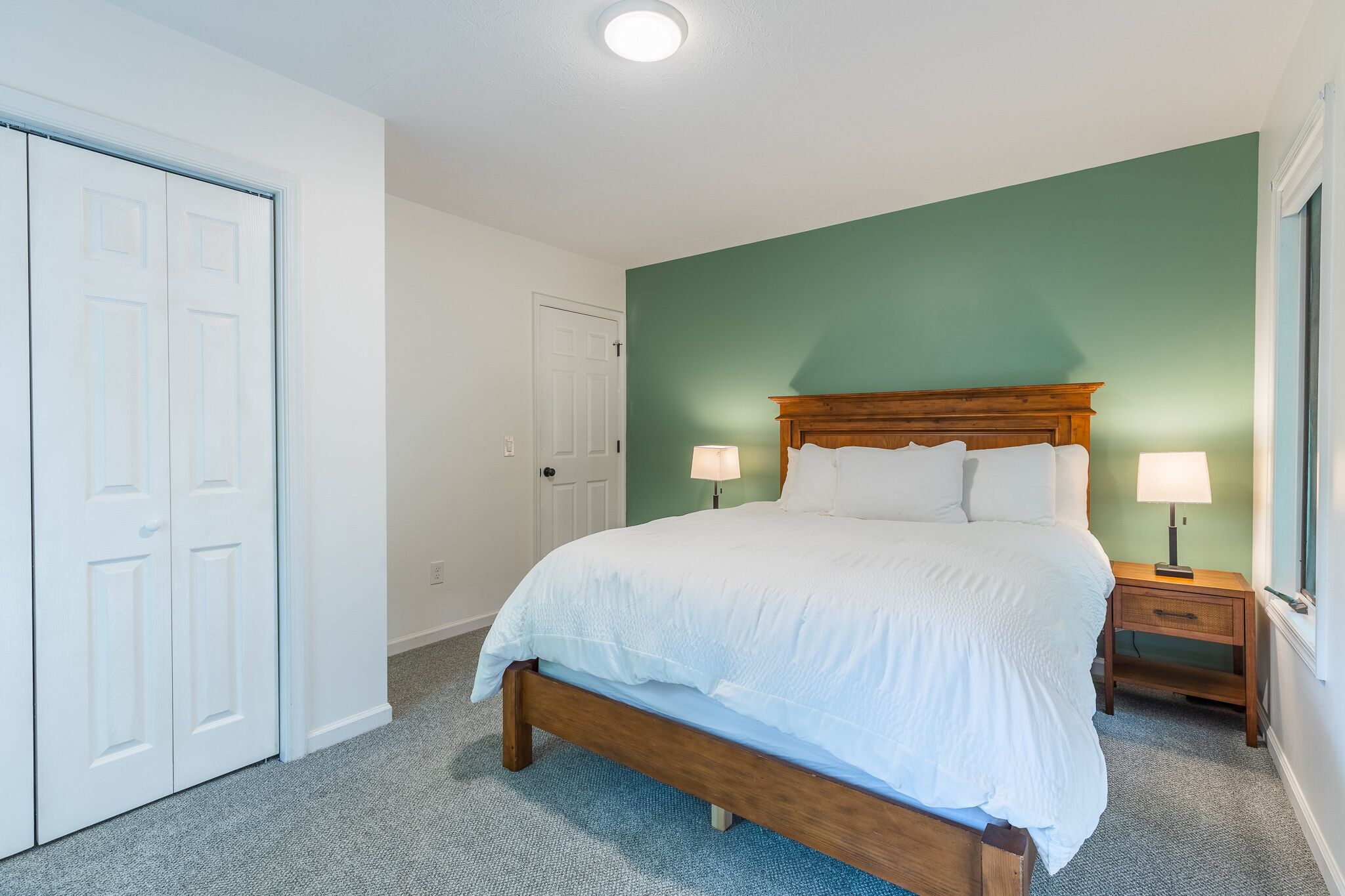 A bedroom with a bed, two bedside tables with lamps, a wardrobe, and a door.