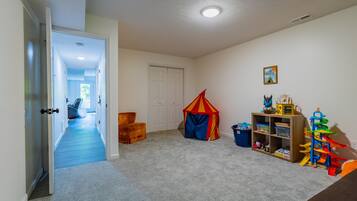 Une salle de jeux pour enfants avec un sol recouvert de moquette, une tente de jeu, une bibliothèque en bois et une porte donnant sur une autre pièce.
