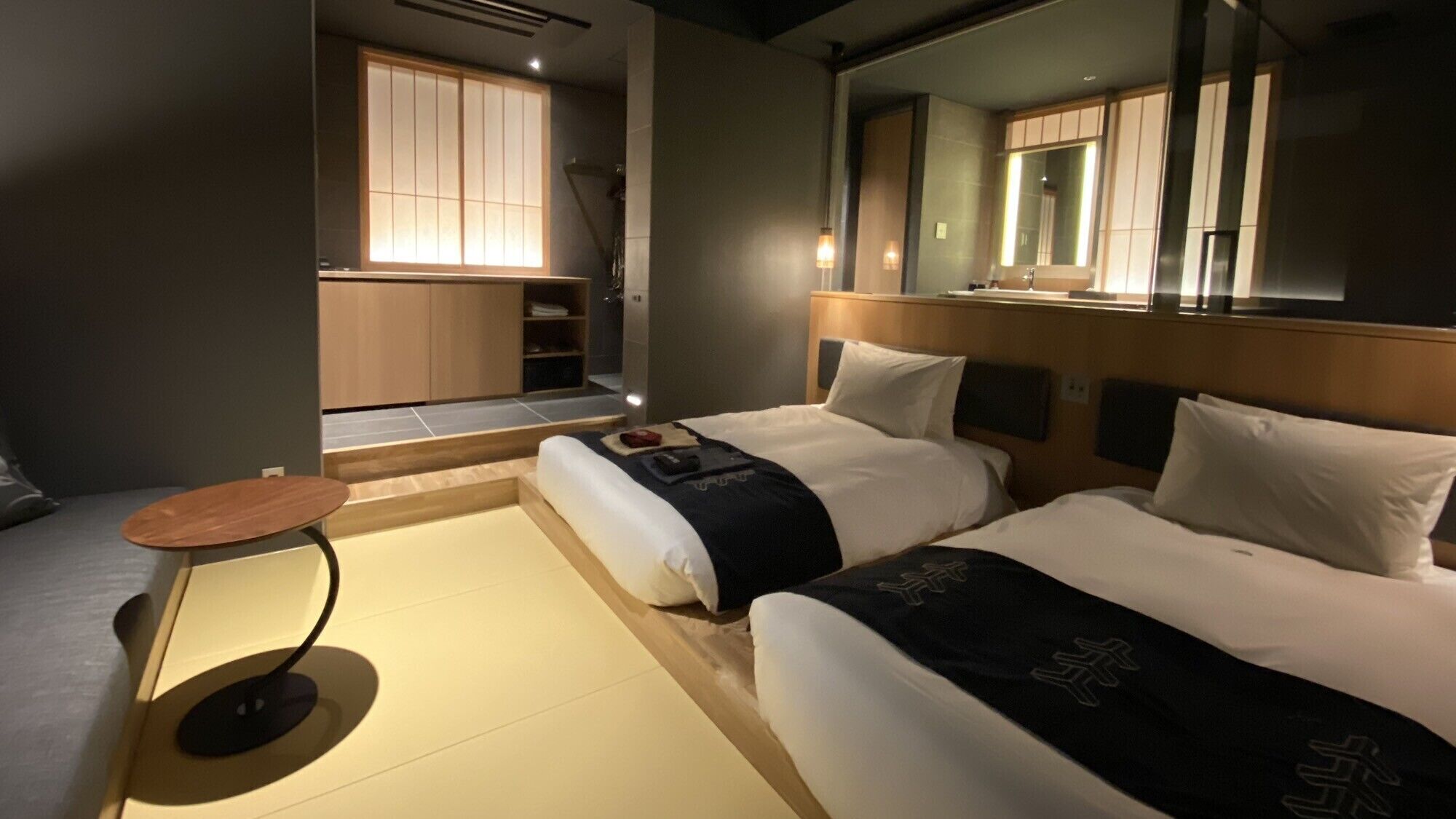 Habitación de hotel con dos camas, una mesita, un espejo y vistas a una puerta corrediza tradicional japonesa.