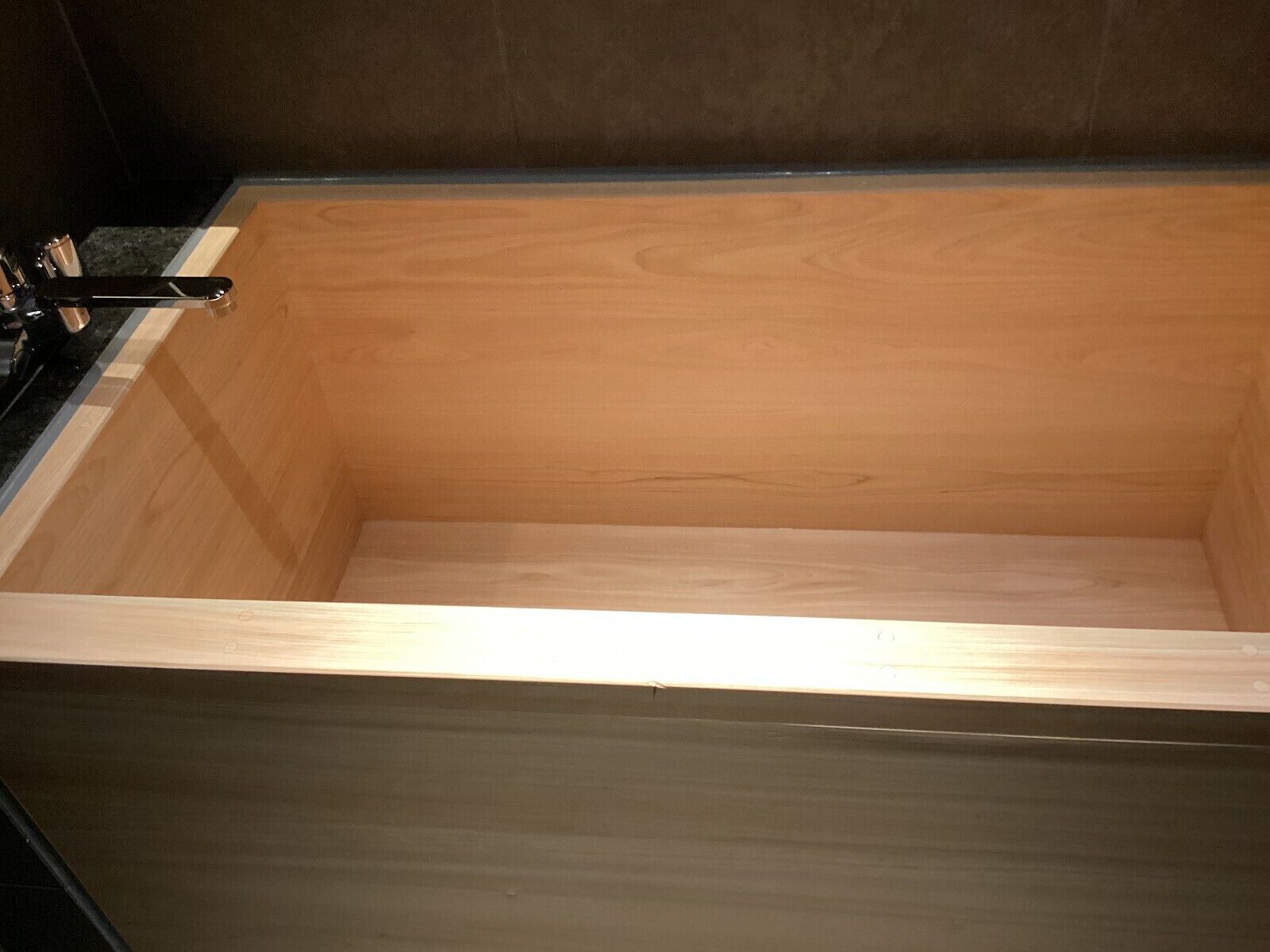 A wooden bathtub with a black faucet and a wooden frame.