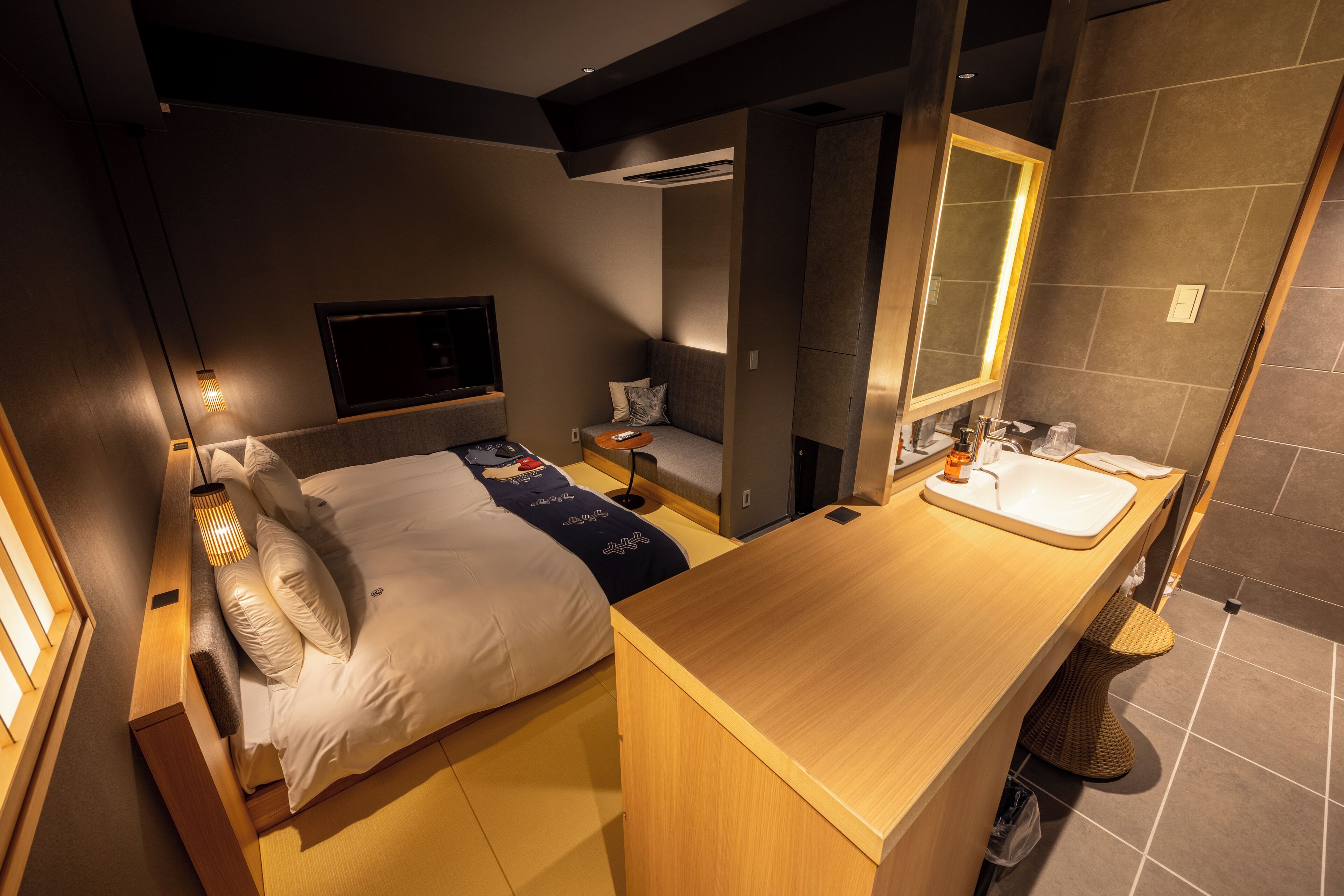 A modern hotel room with a bed, bedside table, and a bathroom with a sink and mirror.