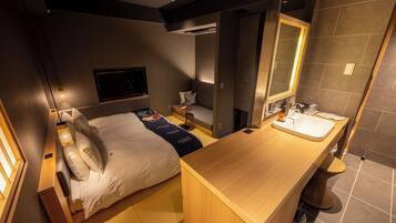 A modern hotel room with a bed, bedside table, and a bathroom with a sink and mirror.