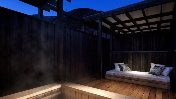 Una terraza de madera con un jacuzzi y una zona de estar con cojines.