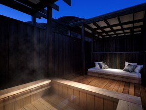 Una terraza de madera con un jacuzzi y una zona de estar con cojines.