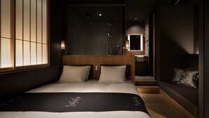 Una habitación de hotel moderna con una cama grande, un cabecero de madera, un baño pequeño con ducha y vistas a la ciudad.
