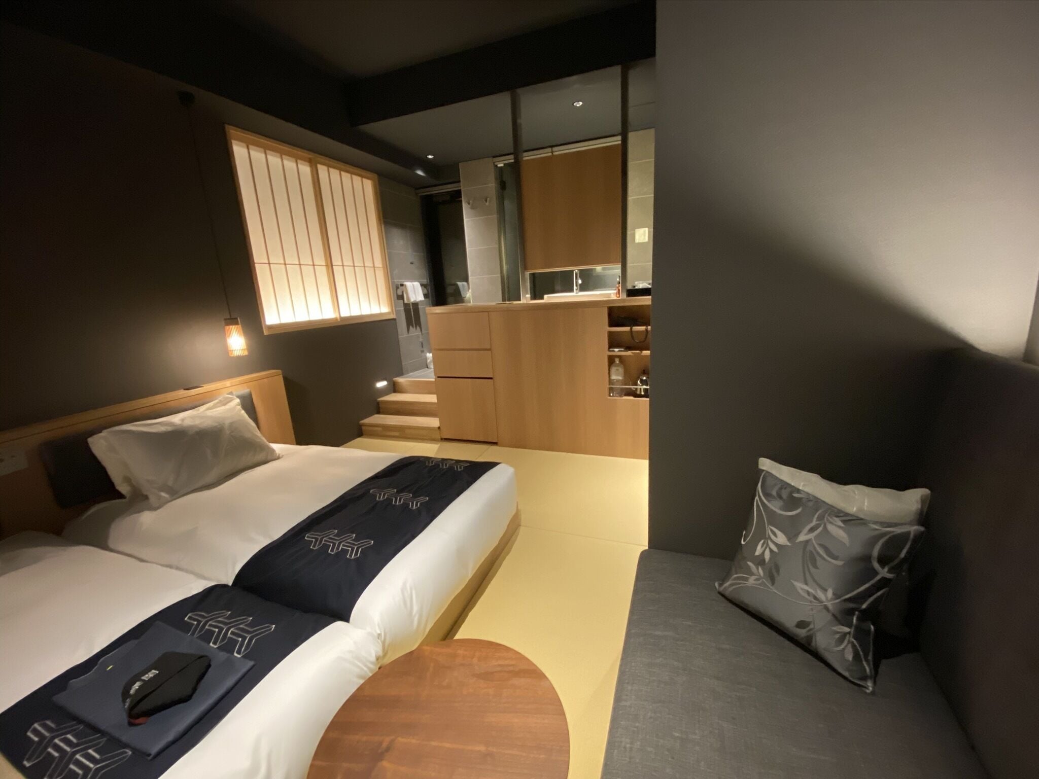 A modern hotel room with a bed, a sofa, a desk, and a kitchenette.