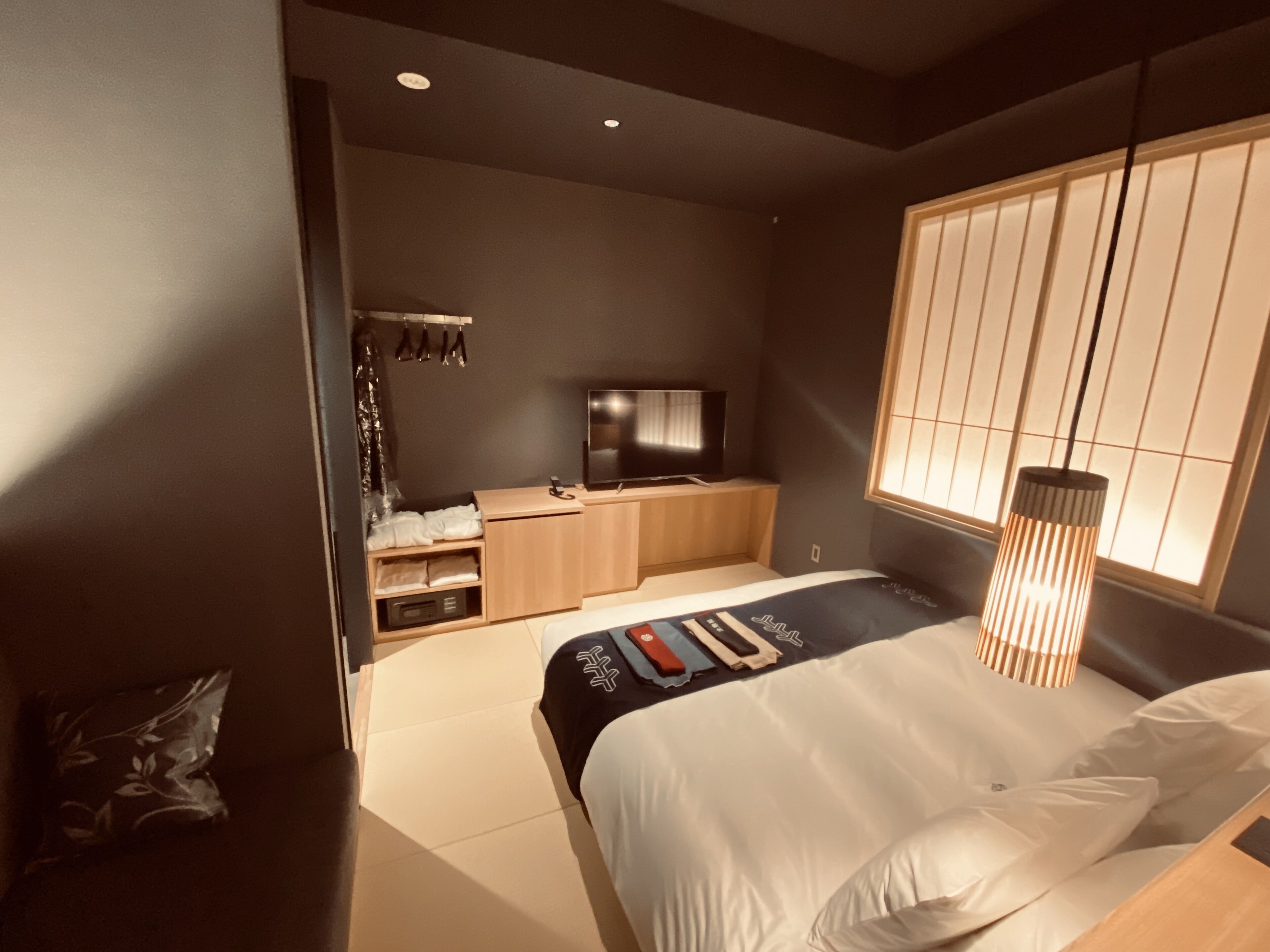A modern bedroom with a bed, bedside table, TV, and a window with blinds.