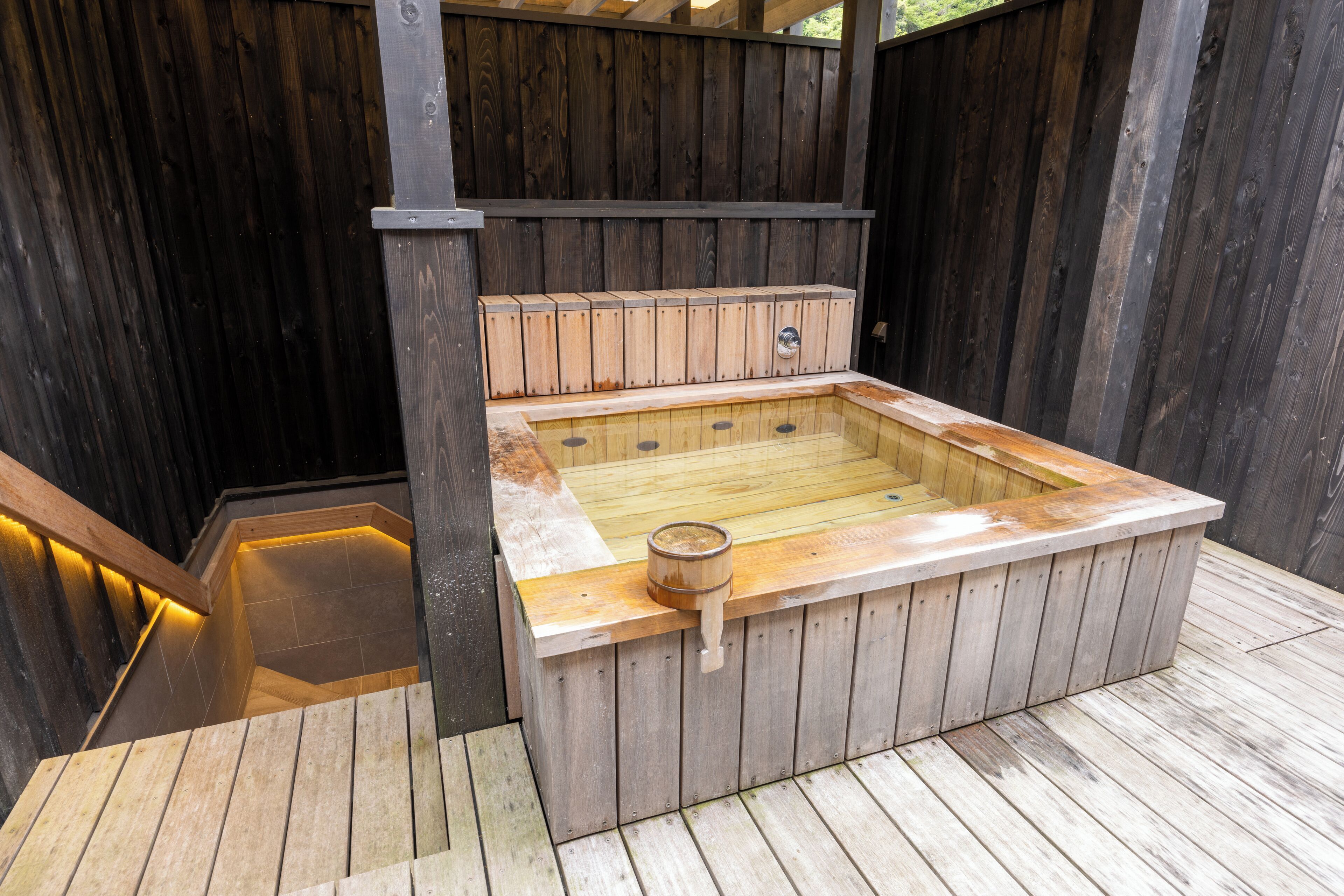 A wooden hot tub with a wooden bench and a wooden bucket.