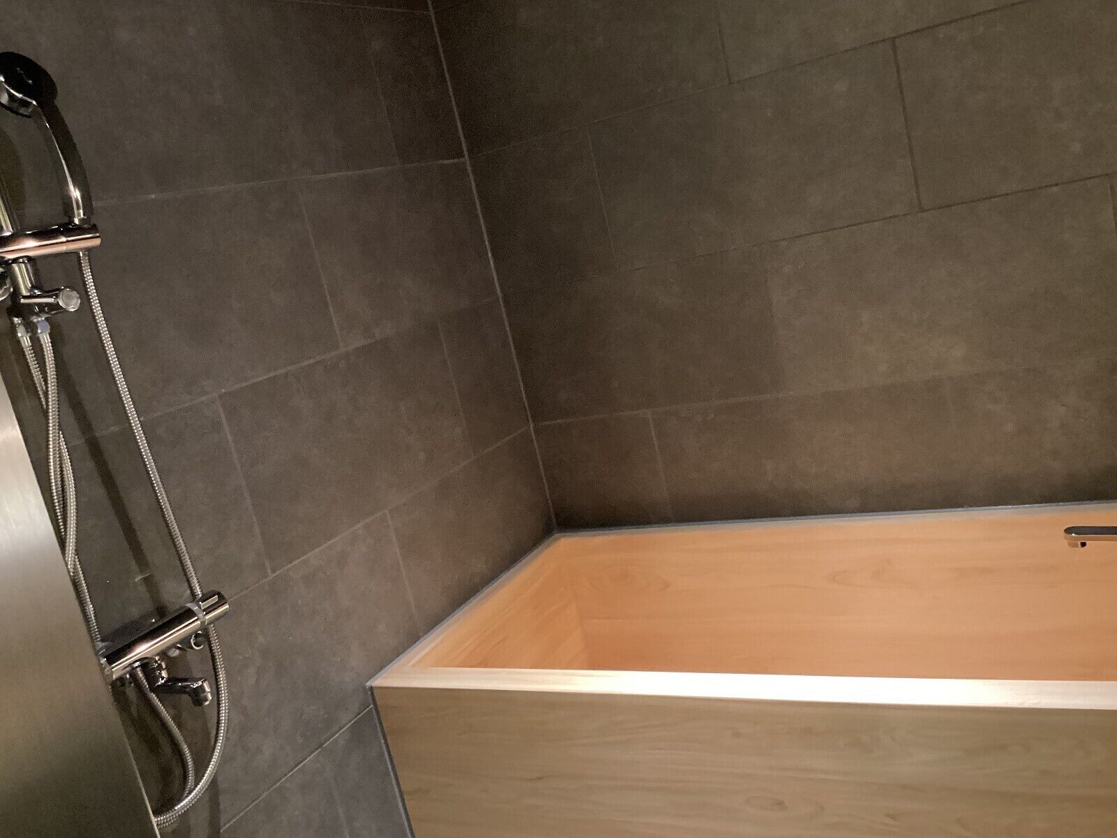 Un coin de salle de bain avec des carreaux sombres et une baignoire en bois.