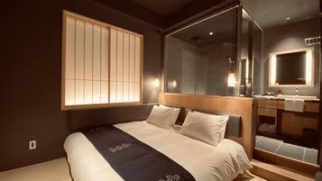 Ein modernes Hotelzimmer mit einem großen Bett, einem Badezimmer mit Spiegel und einem Fenster mit Jalousien.