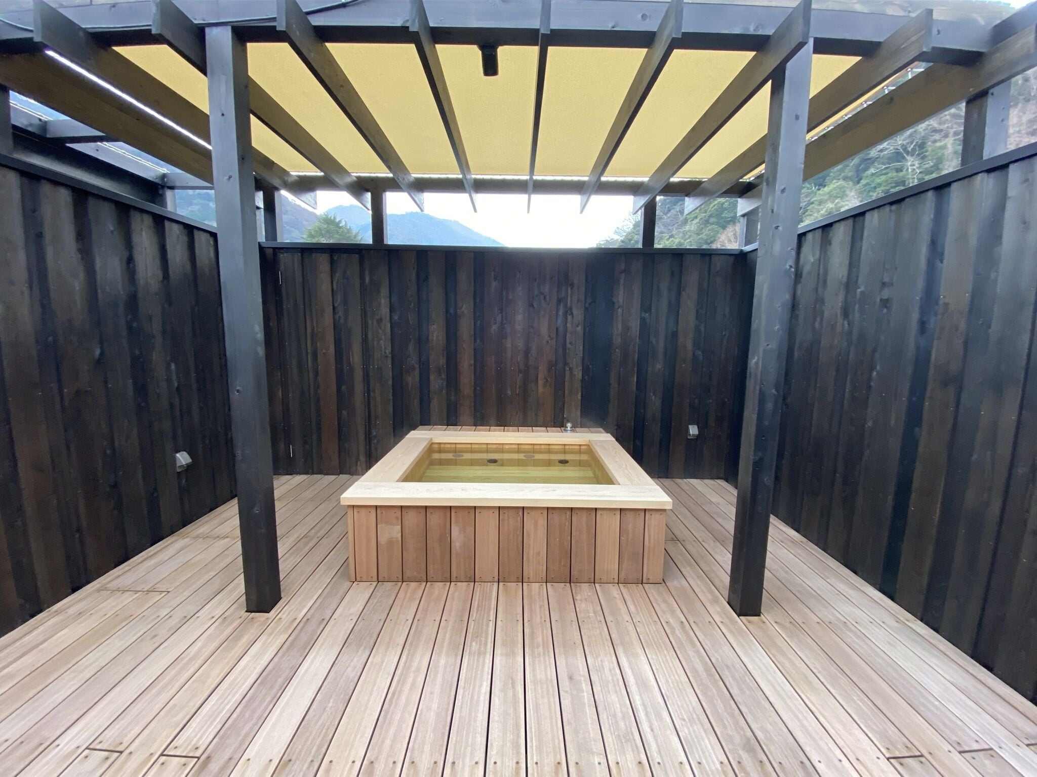 Eine Holzterrasse mit Whirlpool unter einer Pergola.